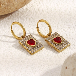 Macro detail of 18K gold plated earring with red heart stone and pavé zircon square pendant
