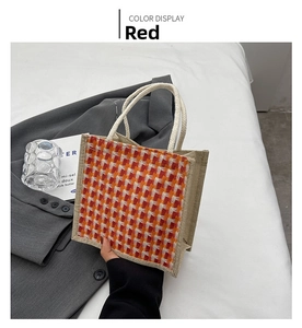 Detail of red and orange plaid linen tote bag with white knot handle on white bedding