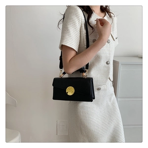 Détail d'un sac carré en cuir noir avec une boucle métallique dorée ronde minimaliste