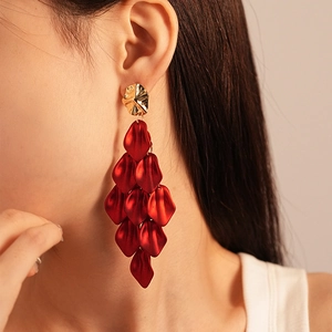Detail of long red acrylic petal tassel earrings with gold studs worn by a model