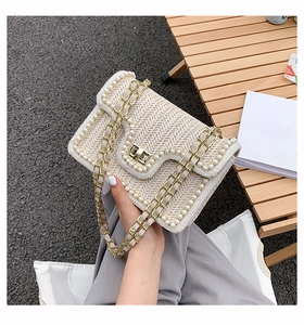Detail of straw woven bag with white pearl trim, golden twist lock and chain strap