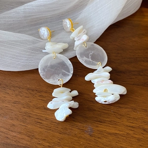 Detailed close-up of shell drop earrings with golden accents on dark wood background