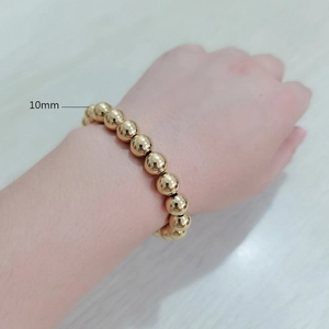 Detail showing a 10mm golden beaded elastic bracelet with a smooth metallic finish