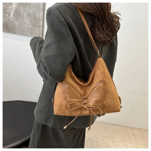 Detail of a brown suede tote bag featuring butterfly embroidery and ribbon tie details