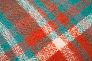 Close-up of thick plaid knit scarf texture with red-orange and green woven wool fibers