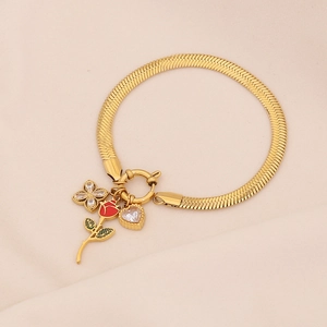 Detail of gold snake chain bracelet with rose, clover, and heart charms on soft fabric