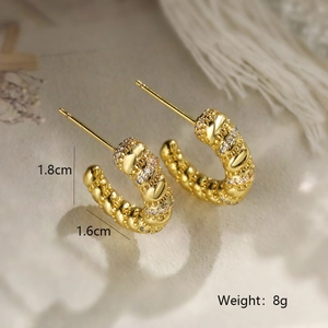 Macro shot of gold plated C-shaped earrings with textured surface and cubic zirconia details