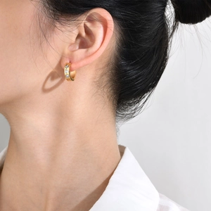 Close-up of a gold-plated hoop earring with three clear zircons worn by a model