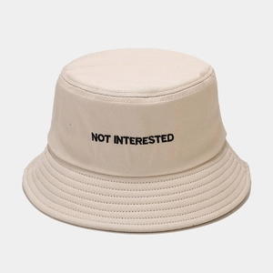 Dettaglio del ricamo NOT INTERESTED su un cappello alla pescatora beige in cotone tela