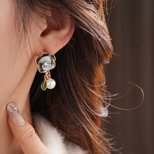 Close-up of model wearing floral pearl drop earrings with blue enamel and gold finish
