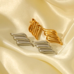Minimalist 18k gold and silver angel wing stainless steel earrings on beige silk fabric
