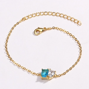 Détail du bracelet doré avec pierre bleue taille émeraude et zircon en forme de cœur