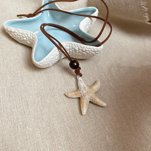 Starfish pendant necklace with brown cord and wooden bead on a blue ceramic dish
