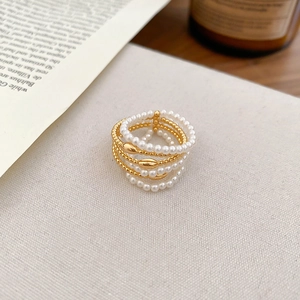 Macro shot of multilayer gold-plated rings with white pearls and beads on textured linen