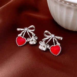 Détail de boucles d'oreilles nœud argentées avec pendentif cœur rouge et petit ours 3D