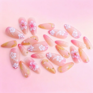 Pink gradient almond press-on nails with 3D white flowers, gold foil, and pearl accents