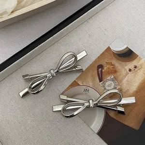 Macro shot of silver metal bow hair clips on grey linen with retro background