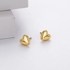 Macro shot of polished gold heart stud earrings on a minimalist white display