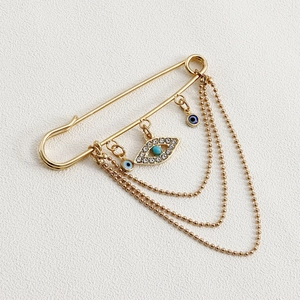 Detailed view of golden evil eye brooch with layered bead chains and rhinestone accents