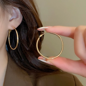 Detail view of large gold hoop earrings showing sleek circular design and lobe fit