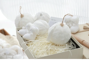 Detail view of white plush Christmas ornaments and knitted boots in a gift box