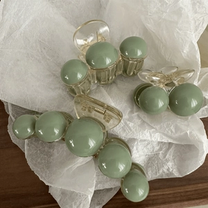 Detailed view of green and transparent spherical pearl hair claws on white paper