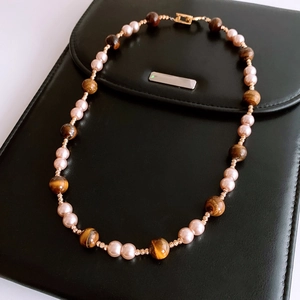 Close-up of pearl and tiger eye beaded necklace on black leather texture