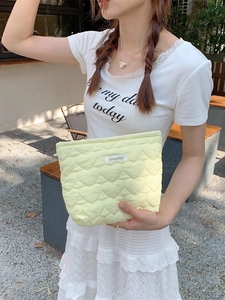 Quilted heart pattern makeup pouch in pale yellow held by a model in natural light