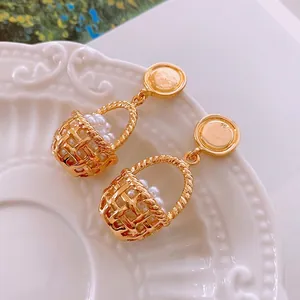 Vintage gold basket earrings featuring woven texture and white faux pearls in white ceramic dish