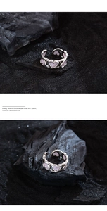Close-up of a silver open heart ring with pink enamel detail on a dark stone background