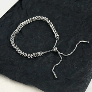 Detail of silver woven titanium steel bracelet with adjustable slide clasp on black background