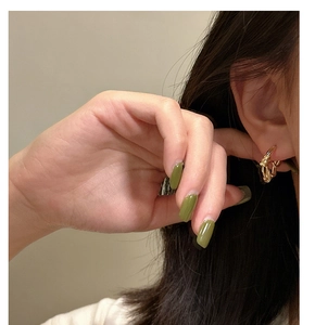 Close-up of golden twisted rope knot hoop earrings worn by a model in a natural setting