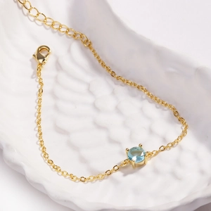 Detailed macro view of a gold bracelet featuring a round light blue stone in 4-prong setting