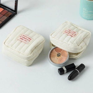 Nahaufnahme cremefarbener gesteppter Kosmetiktaschen mit Make-up auf weißem Tisch
