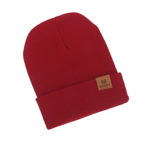 Close-up of a stylish red knitted beanie featuring a brown leather M logo patch detail.