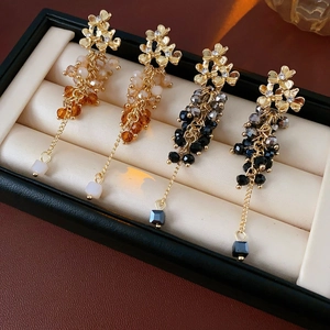Detail view of floral tassel earrings with orange and black beads in a jewelry box