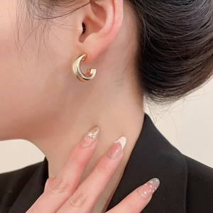 Detailed close-up of a gold-plated C-shaped hoop earring with fine horizontal texture