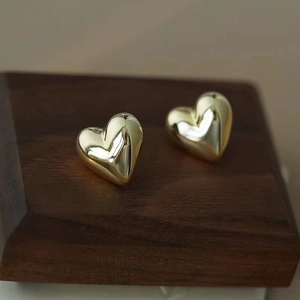 Detailed close-up of polished golden heart-shaped stud earrings on a wooden stand