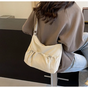 Model wearing a cream nylon pleated crossbody bag with drawstring side pocket details
