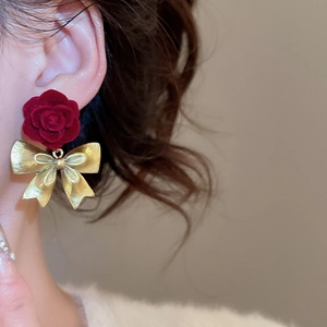 Close-up of burgundy flocked rose earrings with golden metal bowknot on ear lobe