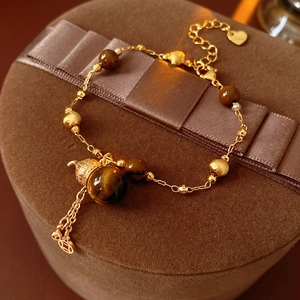 Makroaufnahme von Tigerauge-Perlen, Goldanhängern und Quastendetails an einem Armband