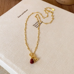Detailed view of the 18k gold plated chain with red bead and bell on a cream book