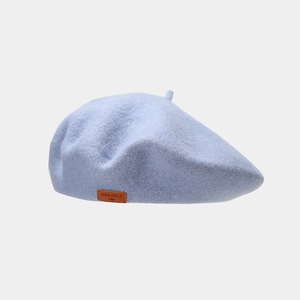 Close-up of light blue wool beret featuring a vintage brown leather label detail