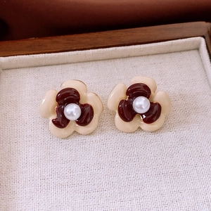 Detail view of flower earrings with cream petals, burgundy enamel, and white pearls