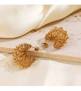 Detailed view of golden twisted coil C-shaped earrings on elegant beige silk and stone