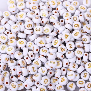 Close-up of white acrylic round beads with golden numbers for DIY jewelry making