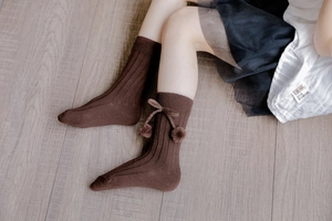 Detail of dark brown knee-high baby socks with knit stripes and plush pom-poms
