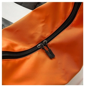 Detail of smooth double metal zippers on vibrant orange nylon dumpling bag surface