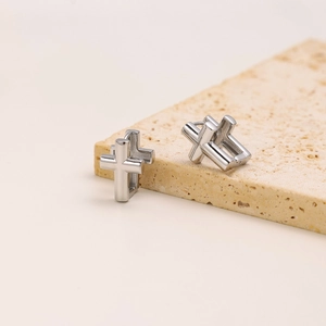 Close-up of silver stainless steel cross hoop earrings on a beige textured stone base