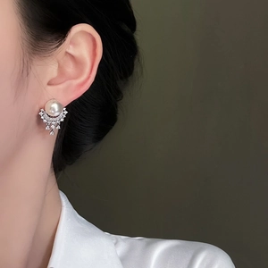 Close-up of pearl earrings with fan-shaped rhinestones on a model wearing white satin